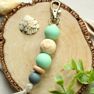 Schlüsselanhänger mit Ankermotiv auf Holzscheibe, neben Sukkulente und Muscheln.