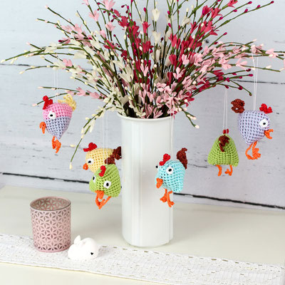 Bunter Blumenstrauß mit gehäkelten Hühnern in einer Vase, umgeben von Kerze und weißem Hasenfigur.