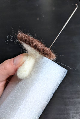 Hand holding mushroom to the foam block and poking felting needle from the top