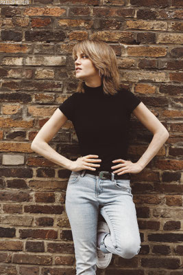 photo de plein pied de Emilie de preissac face a un mur en brique rouge