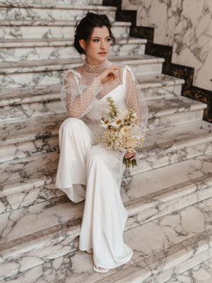 braut mit jumpsuit auf marmortreppe sitzens 