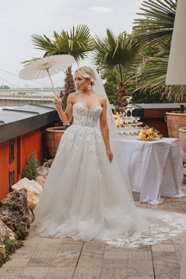 braut in langem kleid auf terrase mit weißem papierschirm