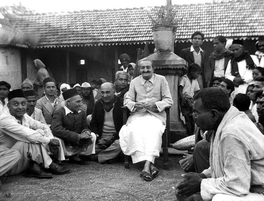 7th Nov.  Meher Baba at the Harijan dharamshala.  Baba's men Mandali are on the left, Bhagirath Tiwari (standing in jacket), Dattu Mehendarge, Sadashiv Patil( black cap & scarf), Eruch J.Photo taken by Panday.