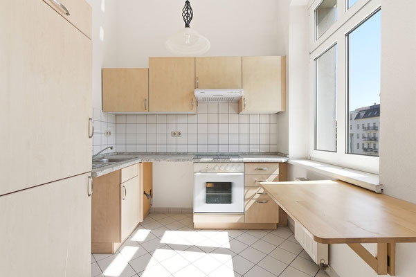 Separate Küche der 1-Zimmer-Wohnung in Prenzlauer Berg mit Fenster, Herd, Kühlschrank und Sitzmöglichkeit