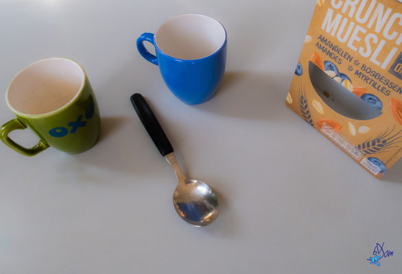 2 tasses et une cuillère, voici un visage en pleine discussion avec une boîte de muesli