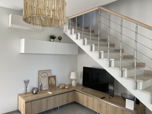 Helles Wohnzimmer mit einer Holztreppe und einem Fernseher, stilvoll und modern eingerichtet.