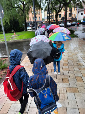 Die Klasse läuft mit Schirmen durch den Regen ins Theater.