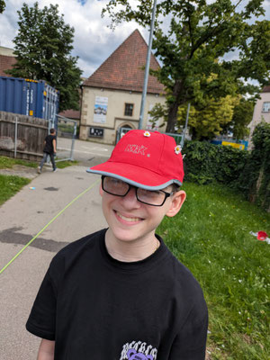 Ein Schüler trägt eine rote Kappe in die Gänseblümchen gesteckt sind.