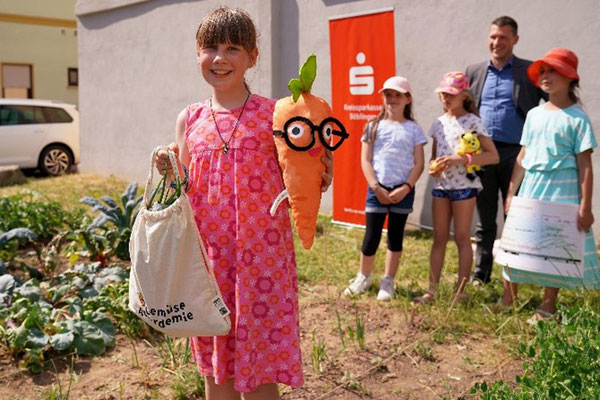 Eine Schülerin präsentiert eine Stofftiermöhre und eine Tasche voller Gemüse.