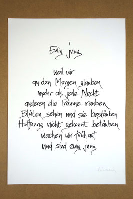 Vollansicht Kalligrafie „Ewig jung“ Tusche auf Papier vor Hintergrund einer Tischplatte