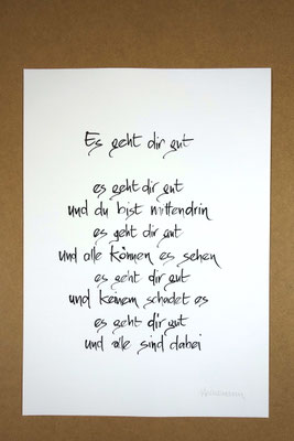 Vollansicht Kalligrafie „Es geht dir gut“ Tusche auf Papier vor Hintergrund einer Tischplatte