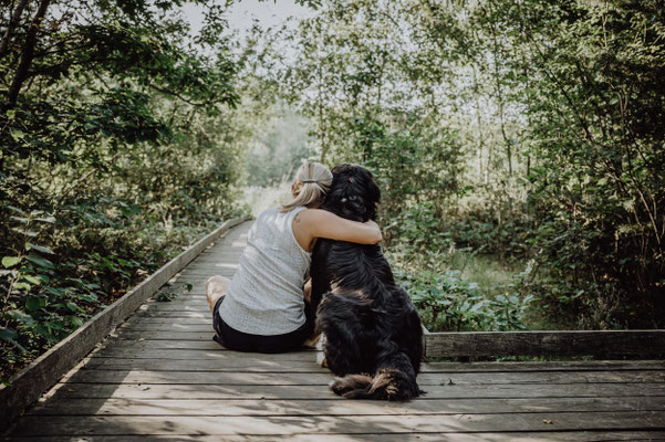 Frau mit Hund von hinten auf einem Holzsteg