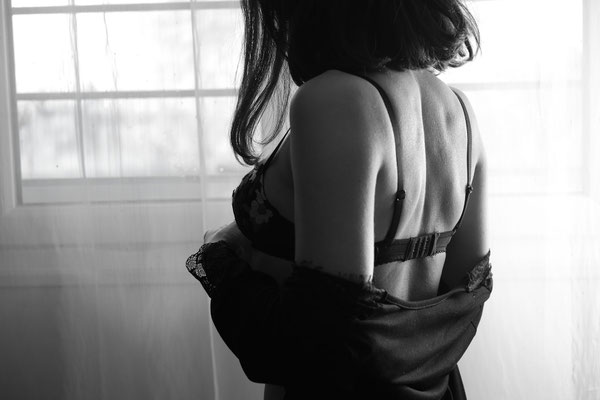 femme brune en lingerie de dos devant une fenêtre