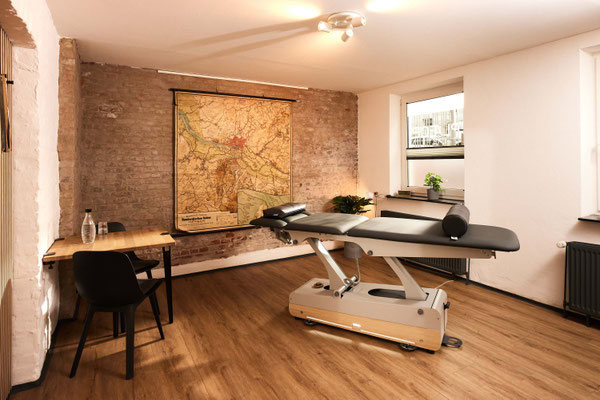 Therapieraum mit höhenverstellbarer Behandlungsliege vor freigelegter Backsteinwand, in ruhiger, warmer Atmosphäre im PLÆCE ØNE Therapy CoWorking Hamburg