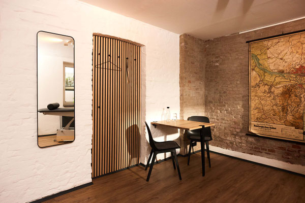 Blick in den Behandlungsraum mit Spiegel, Holztisch vor der freigelegten Backsteinwand mit Hamburger Stadtkarte; eine ruhige, freundliche Atmosphäre im PLÆCE ØNE Therapy CoWorking Hamburg