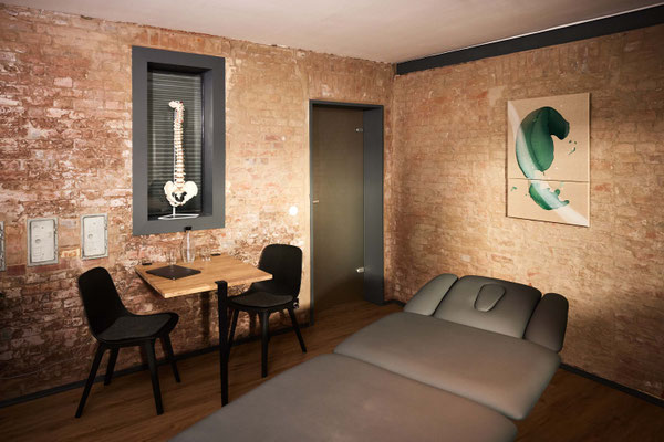 Ruhiger Behandlungsraum mit Therapieliege vor freigelegter Backsteinwand und Kunst an der Wand im PLÆCE ØNE Therapy CoWorking Hamburg