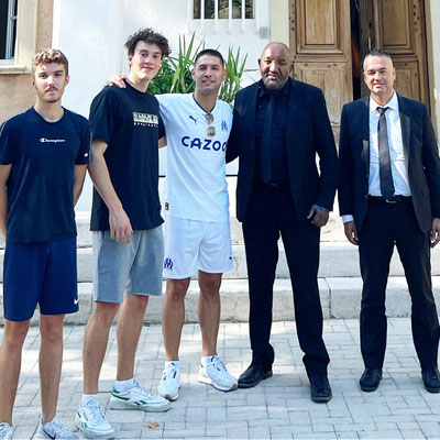 Fußball-Freestyler Saki im Olympique-Marseille-Trikot posiert mit mehreren Personen vor einem Gebäude des Vereins