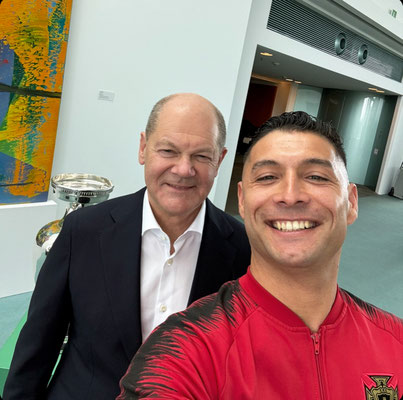 Selfie von Saki mit Olaf Scholz im Anzug vor EM-Pokal und modernem Kunstwerk im Bundeskanzleramt