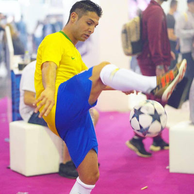 Football freestyler Saki performing ball tricks in a yellow jersey.