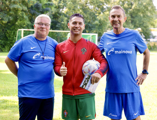 Fußball-Freestyler Saki steht zwischen Trainern auf dem Sportplatz beim Mainova Fußballcamp