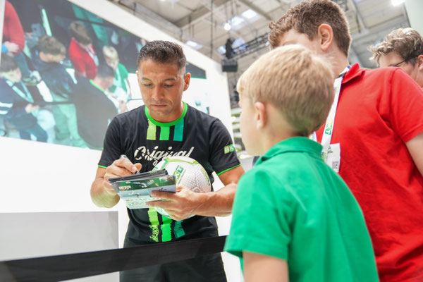Saki gibt einem Kind am BKT-Stand auf der Agritechnica 2025 ein Autogramm