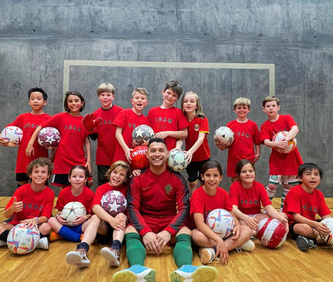 Children's indoor group photo with footballs and coach after training session