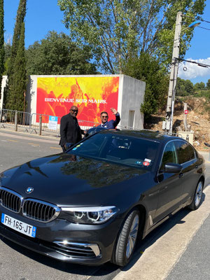 Saki bei der Ankunft bei Olympique Marseille neben schwarzem BMW vor Begrüßungswand