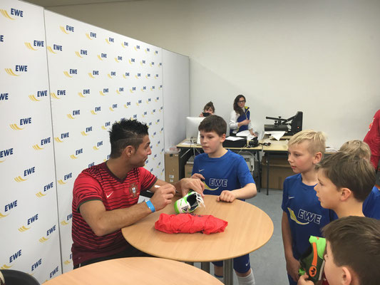 Saki spricht mit Jugendspielern und signiert einen Schuh vor der EWE-Sponsorenwand – Turnier-Highlight beim EWE Cup 2016.