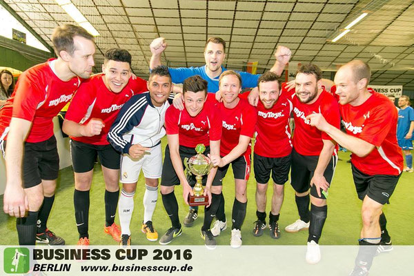 Jubelndes Siegerteam in roten Trikots beim Business Cup Berlin – Pokal und Saki im Bild.