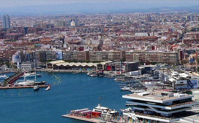 El Puerto de Valencia visto desde el aire muestra una extensa área industrial y comercial que contrasta con el perfil urbano de la ciudad, con un gran número de barcos, grúas y contenedores.
