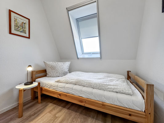 Das zweite kleine Schlafzimmer verfügt über ein Einzelbett mit einem Beistelltisch mit einer Nachtischlampe.  Die Dachschräge mit Fenster sorgen für ein angenehmes Raumklima. 