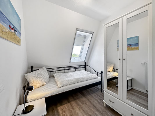 Ein kleines Schlafzimmer mit einem Einzelbett mit einem großem Kleiderschrank. Ein Fenster sorgt für natürliches Licht.
