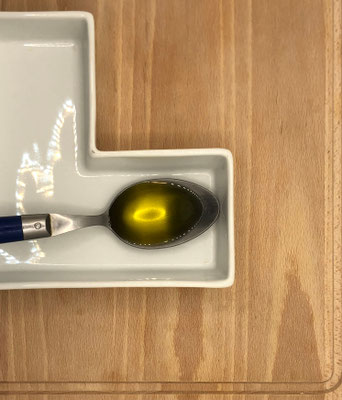 Huile d'olive bio dans sa cuillère en métal vue du dessus sur une planche en bois