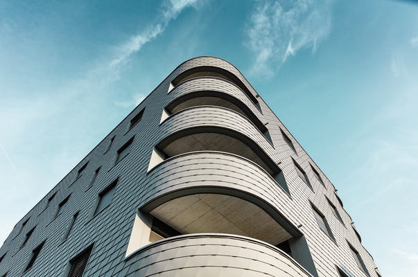 Die Fassade aus kleinteiligen PREFA-Wandschindeln in P.10 Hellgrau verleiht dem Mixed-Use-Building einen aufsehenerregenden Reptilien-Look.