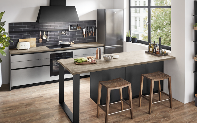 Moderne Küche im Industrial Style mit Kochinsel, Holzarbeitsplatten, schwarzer Rückwand, Edelstahlgeräten und gemütlichem Essbereich – zeitgemäßes Küchendesign mit großen Fenstern und viel Licht.