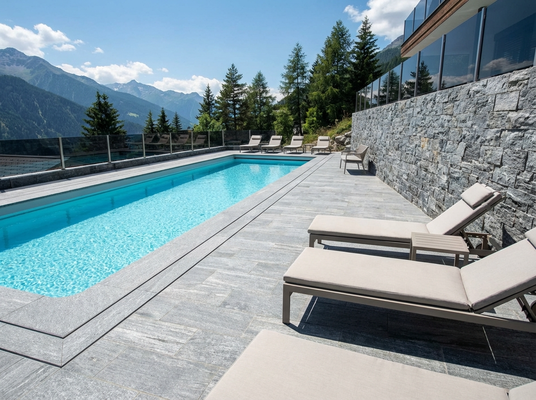 Großzügige, moderne Terrassenlandschaft mit grauen Steinplatten und direktem Übergang zum Außenpool