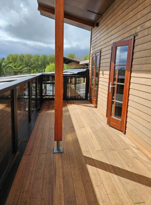 Bambus-Terrassendielen Colon der Closed Decking-Serie montiert auf einem überdachten Balkon mit Glasgeländer und Holzfassade.