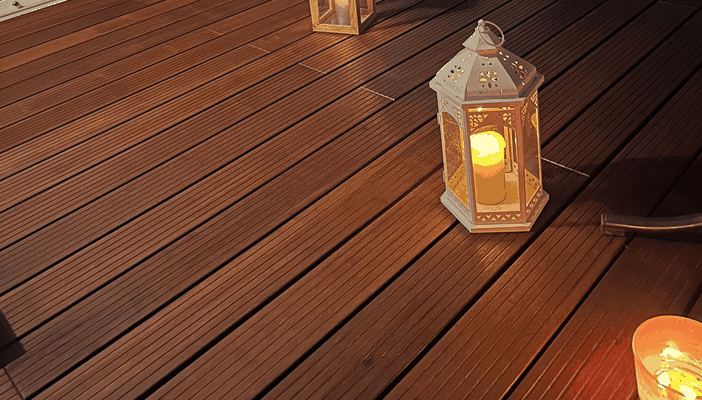 Stimmungsvolle Szene auf einer gepflegten Bambus-Terrasse mit schmaler Riffelung. Mehrere dekorative Laternen mit brennenden Kerzen sorgen für warmes Licht. Die natürliche Holzoptik der Terrassendielen erinnert an Bangkirai, ist jedoch eine nachhaltige Ba