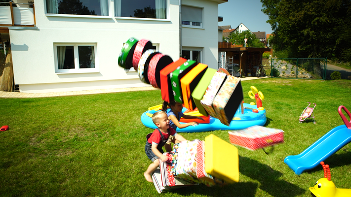 viele bunte Sitzkissen für den Außenbereich, mit denen ein Kleinkind spielt