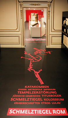 Die jüdischen Grabsteine im Eingangsraum stammen aus den Katakomben in Rom. Die grafische Darstellung einer Katakombe ist als Plot auf dem Fußboden geklebt.