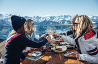 Freundinnen genießen bei den Falstaff Genuss-Skitagen auf der Schmittenhöhe exklusive alpine Spezialitäten in beeindruckender Bergkulisse.