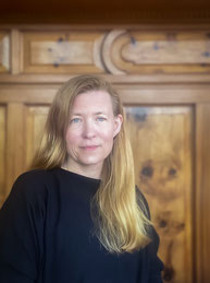 Porträt der Leiterin des Literaturhauses Vorarlberg mit blonden langen Haaren vor holzvertäfelter Wand