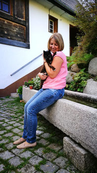 Bild zeigt Svenja Lampke, auf einem Brunnen sitzend mit einer schwarzen Katze auf dem Arm. Das Bild steht symbolisch für das Seminar Tierkommunikation von Svenja Lampke.