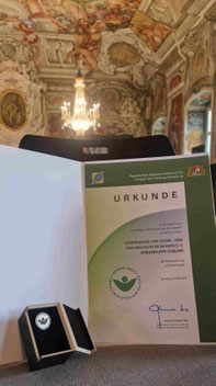 Die Ehrung des Bayerischen Umweltministeriums umfasst eine Auszeichnung und eine Ehrennadel.