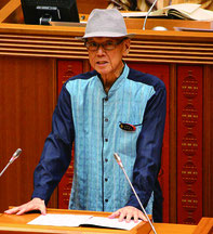議案説明をする翁長知事。議場内での帽子着用は新里議長が許可した=12日、県議会