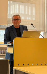 Redner am Pult bei der offiziellen Begrüßung der Teilnehmer:innen