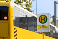 alt="Gelber Linienbus an einer Bushaltestelle mit Haltestellenschild"
