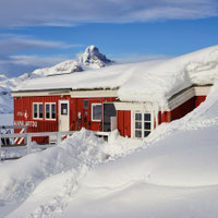L'immagine mostra l'edificio rosso dell'hotel "The Red House" in un paesaggio invernale innevato e con un cielo blu.