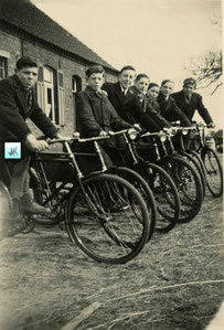 Zeven jongens met een fiets voor een oude boerderij.