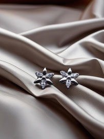 Silver star-shaped stud earrings with clear stones placed on softly folded champagne-colored silk. Elegant minimalist product photo.